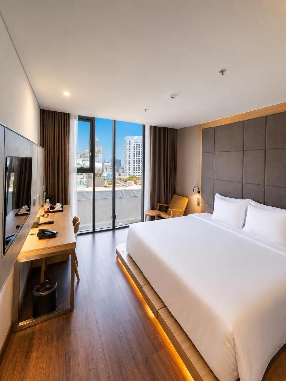 A bright bedroom with a large bed, work desk and glass doors opening toward a city view.
