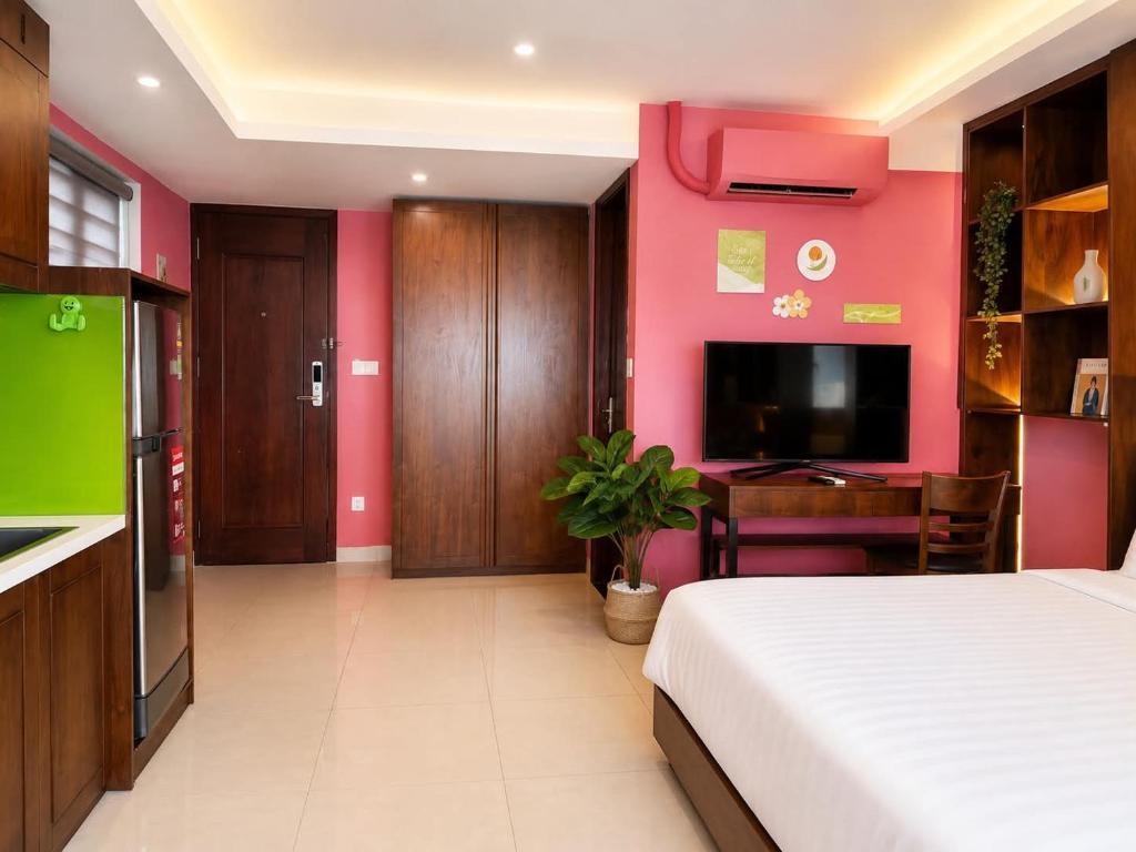 A pink-accented bedroom with a television, dressing desk and kitchenette edge.