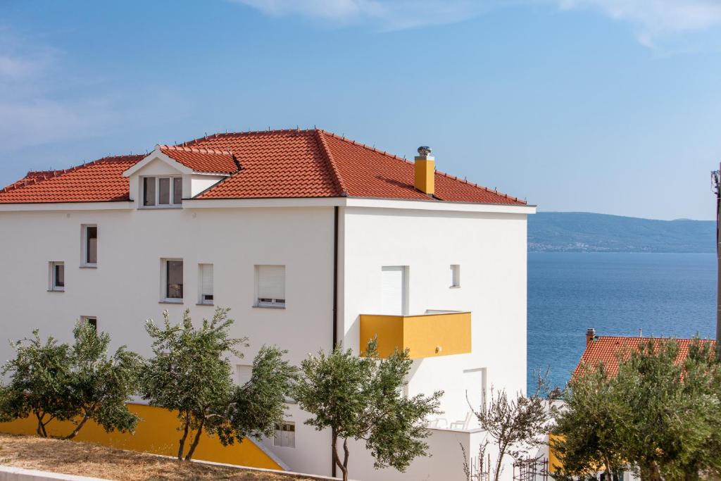 a white building with a red roof next to the ocean at Knezovic Apartments in Podstrana