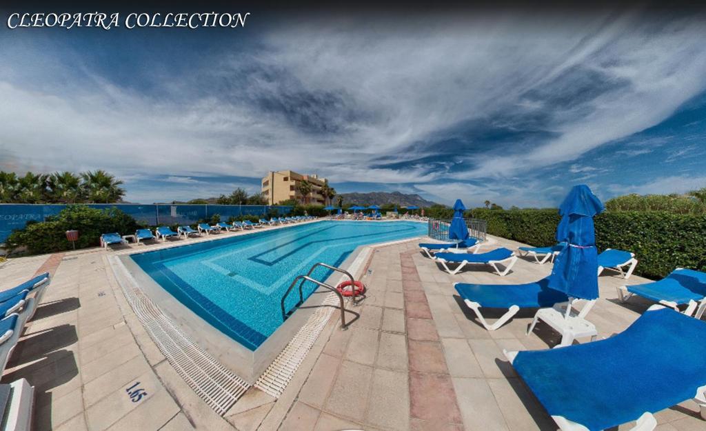 a swimming pool with chairs and blue umbrellas at Cleopatra Superior in Kardamaina