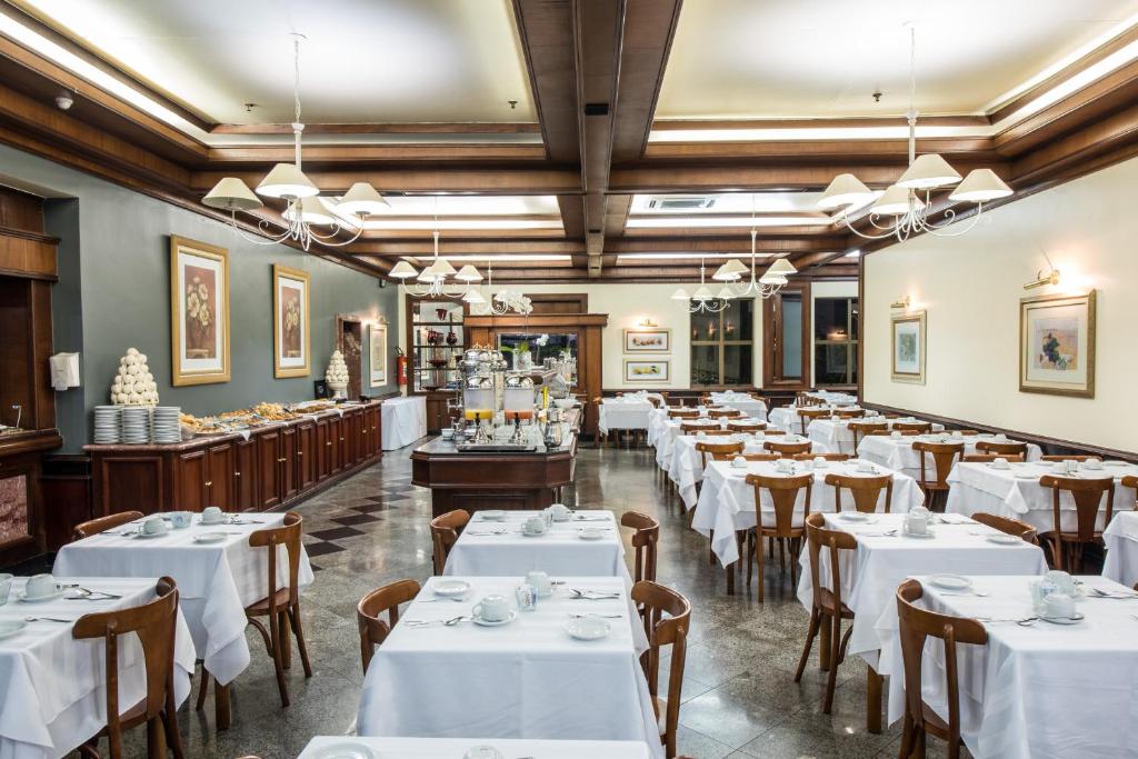 un comedor con mesas y sillas blancas en Hotel Carlton Plaza, en Poços de Caldas