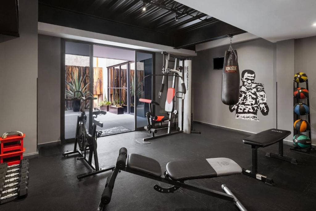 A compact fitness room offers cardio equipment, weight machines, a bench, and a boxing bag.