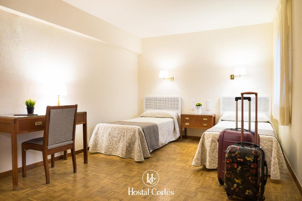 a hotel room with two beds and a desk with a suitcase at Hostal Cortes in Cuenca