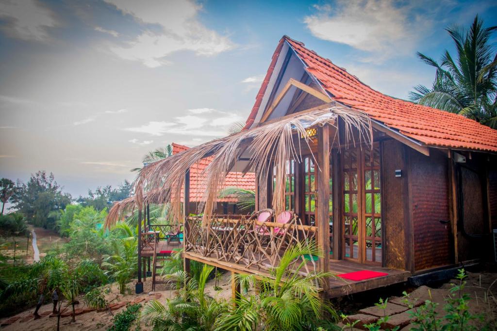 ein Haus mit einem Strohdach und Stühlen darin in der Unterkunft Little India Beach Cottages in Baga