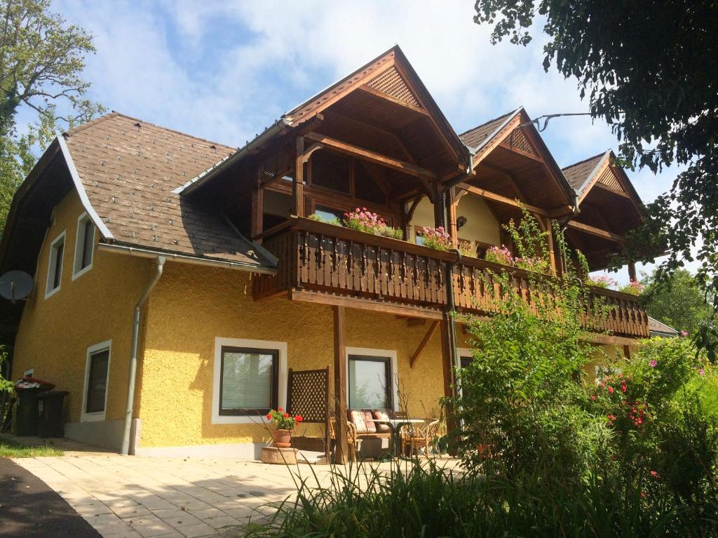 ein gelbes Haus mit einem Balkon mit Blumen darauf in der Unterkunft Singer-Hof in Krumpendorf am Wörthersee