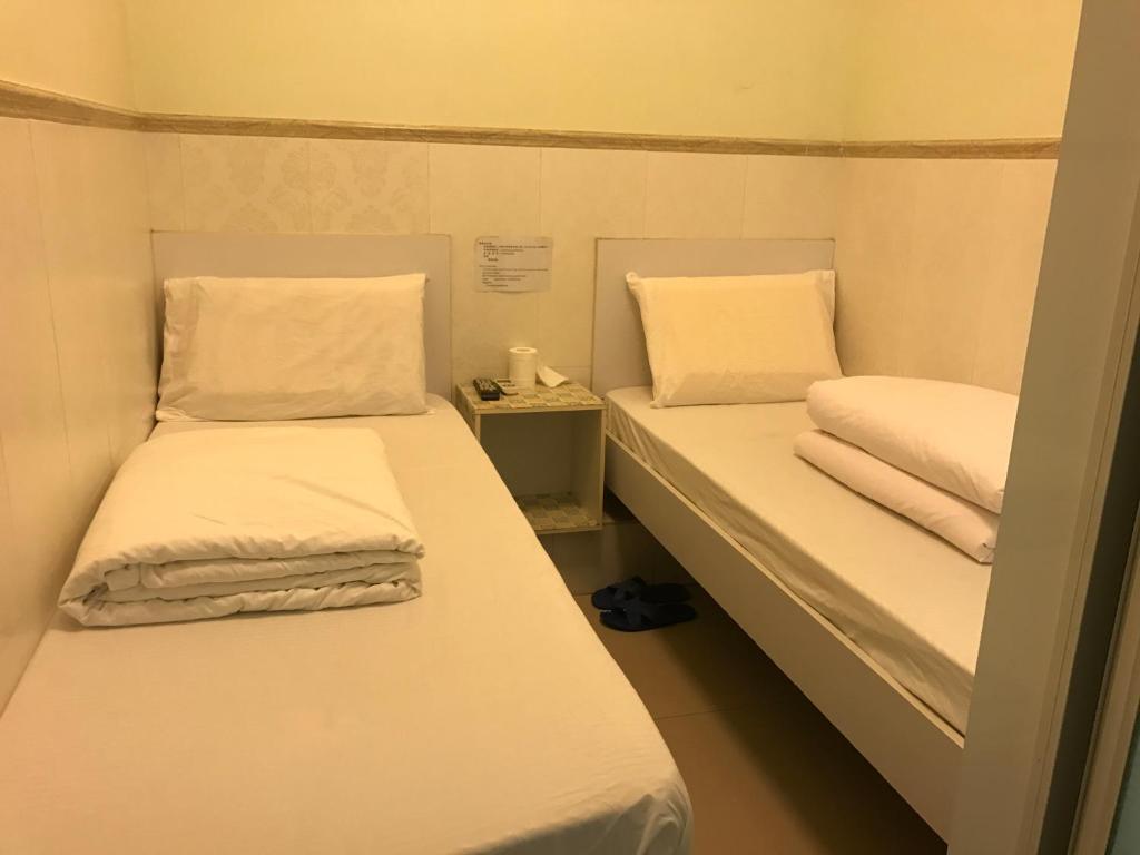 香港にあるビバリー ゲストハウスの小さな部屋のベッド2台(白いシーツ、枕付)