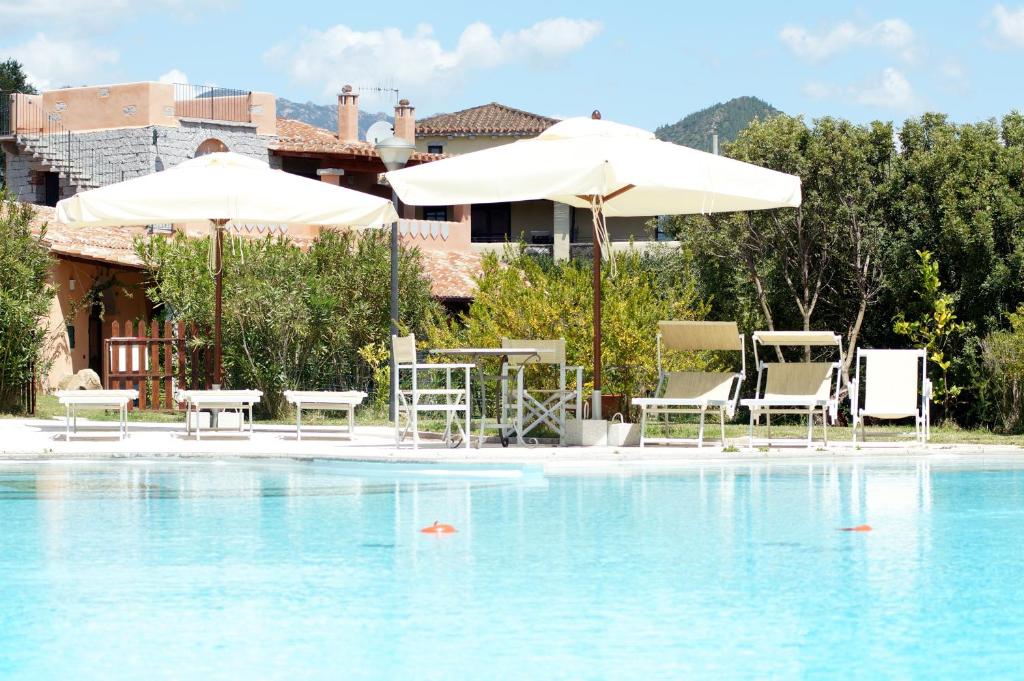 a swimming pool with two umbrellas and chairs and a table at I Mandorli in Lotzorai