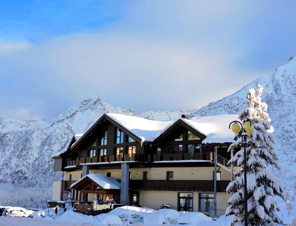 un edificio ricoperto di neve con montagne sullo sfondo di Hotel Adamello a Passo del Tonale