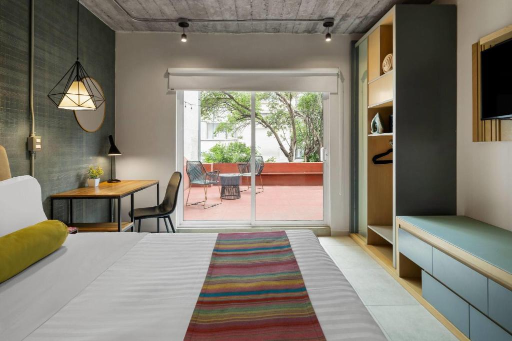 A modern bedroom has a large bed, a compact work table and direct access to a furnished terrace.