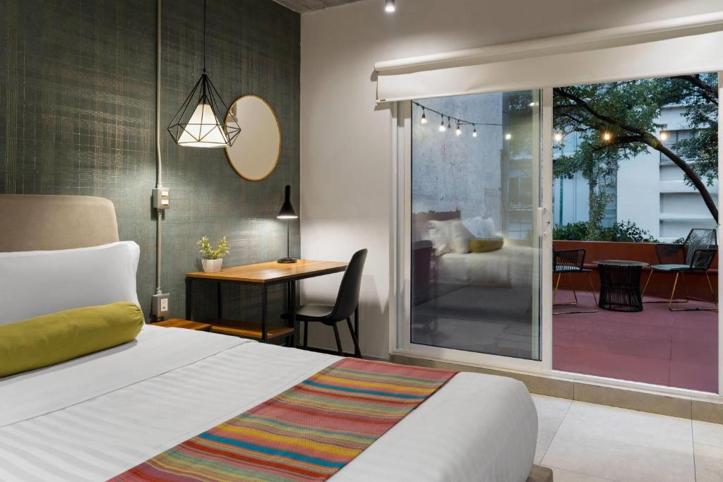 A bedroom with a small desk looks onto a warmly lit terrace through floor-to-ceiling glass.