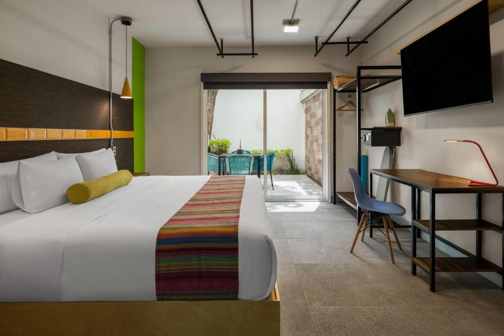 A modern bedroom with a large bed, work desk and glazed outdoor sitting area.
