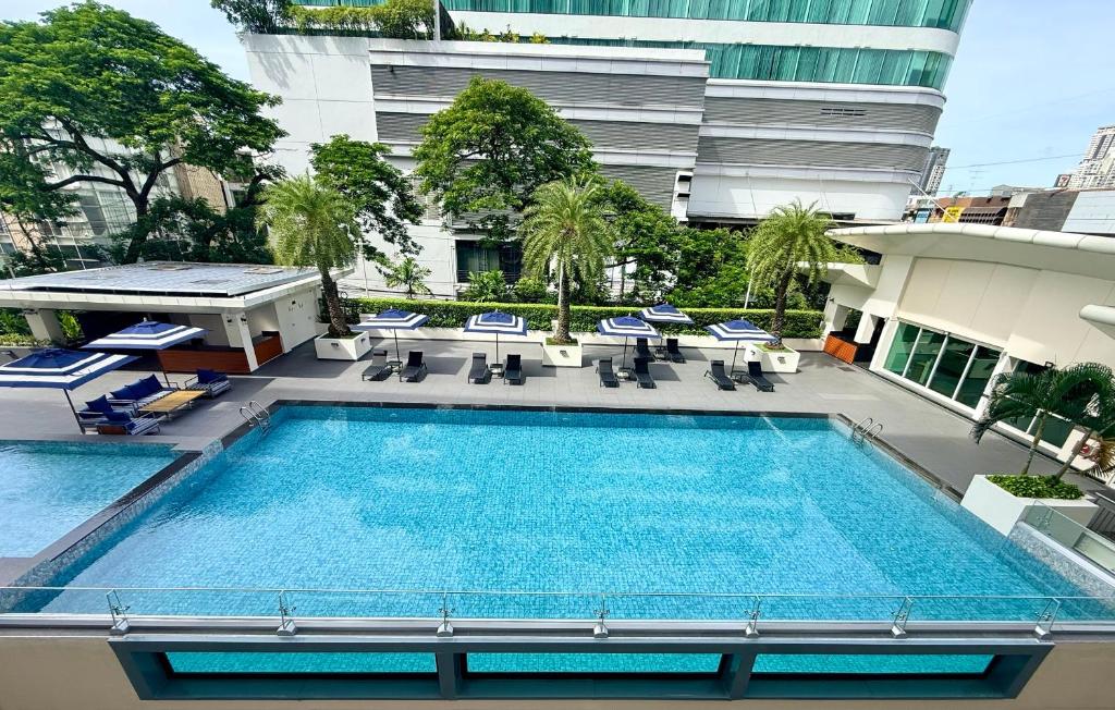 A bright hotel pool framed by loungers, greenery, and surrounding buildings.