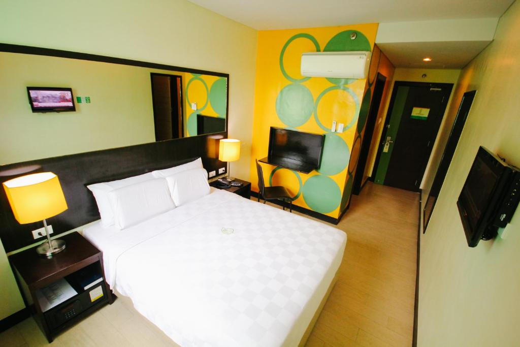 Go Hotels Dumaguete في دوماغيتي: غرفة نوم بسرير ابيض وتلفزيون