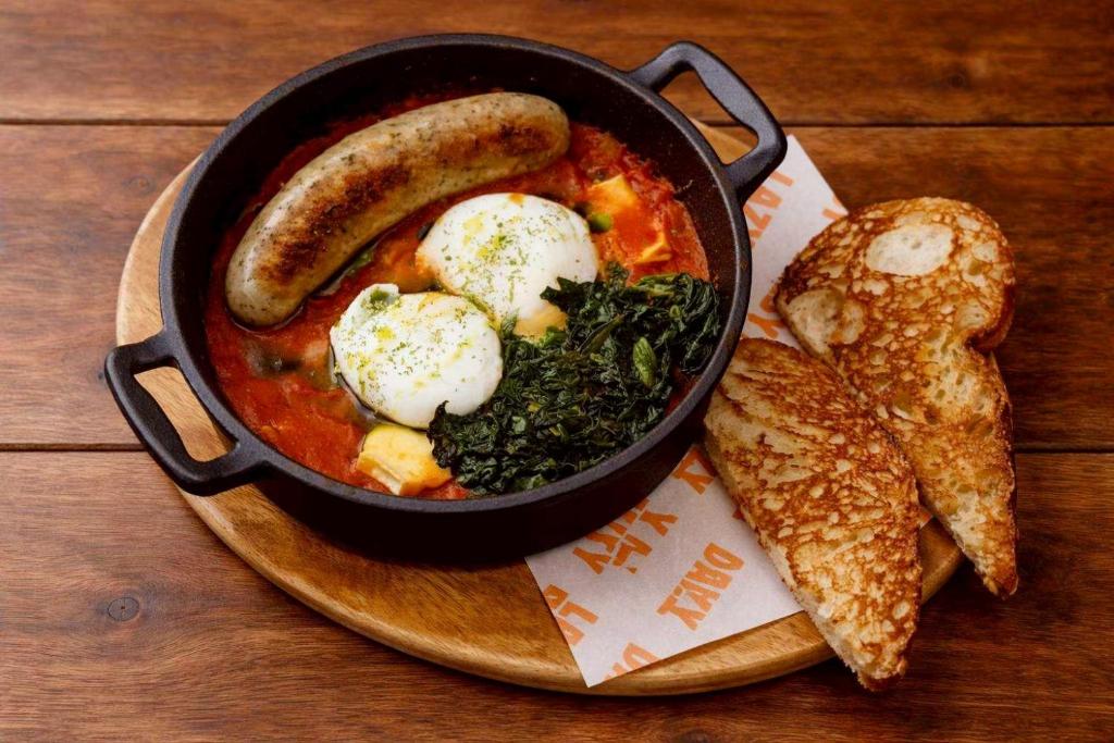 A skillet breakfast with sausage, eggs, greens, tomato sauce, and toast.