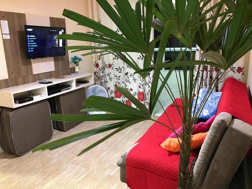 ein Wohnzimmer mit einer roten Couch und einer Palme in der Unterkunft Apartamento no Canto do Forte, Luxuoso e Confortável, 2 Suítes, Varanda Gourmet in Praia Grande