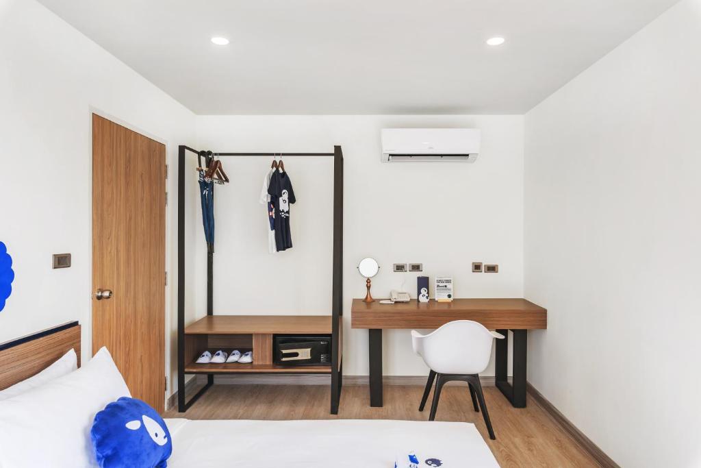 A compact bedroom workspace sits beside an open clothes rail and a bed.