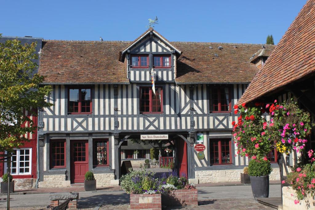 een oud zwart-wit gebouw met rode deuren en bloemen bij Aux Trois Damoiselles in Beuvron-en-Auge