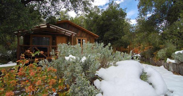a snow covered garden in front of a log cabin at Cabañas Parque Almendro in San José de Maipo