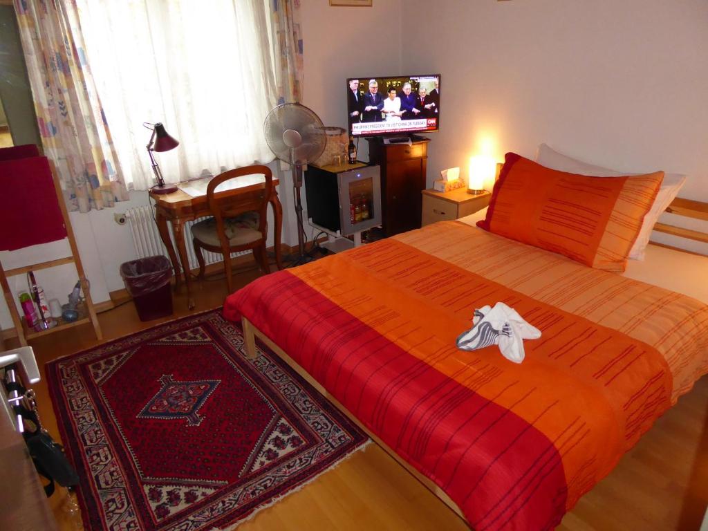 a bedroom with a bed with a red blanket and a television at B&B Pappelweg - 2 in Muttenz