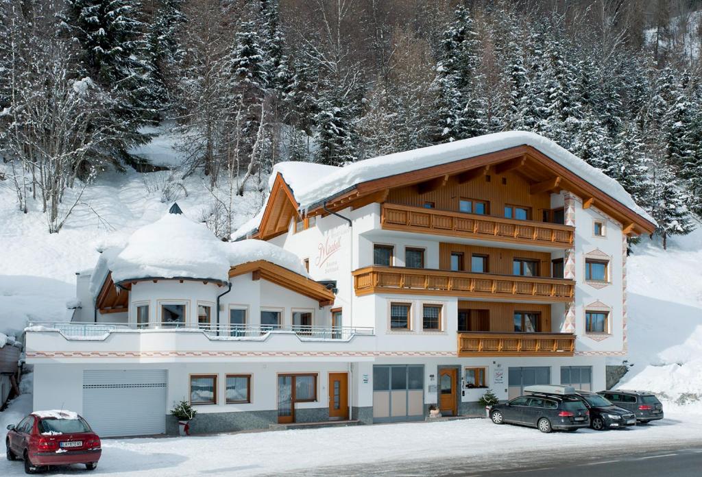 un gran edificio con coches aparcados en la nieve en Apart Garni Mirabell, en Kappl