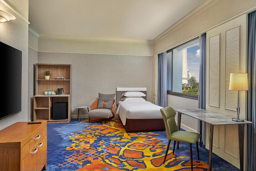 A bright room with a double bed, two chairs and a window-side desk.