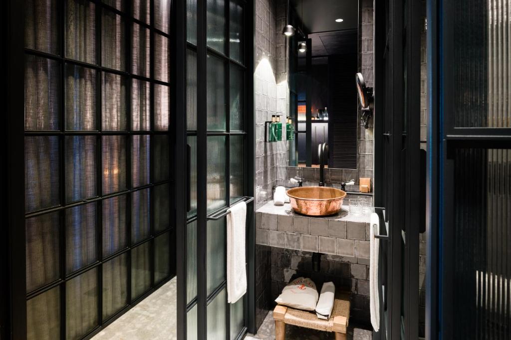 A narrow, dark-tiled bathroom with a copper-toned basin beneath a large window.