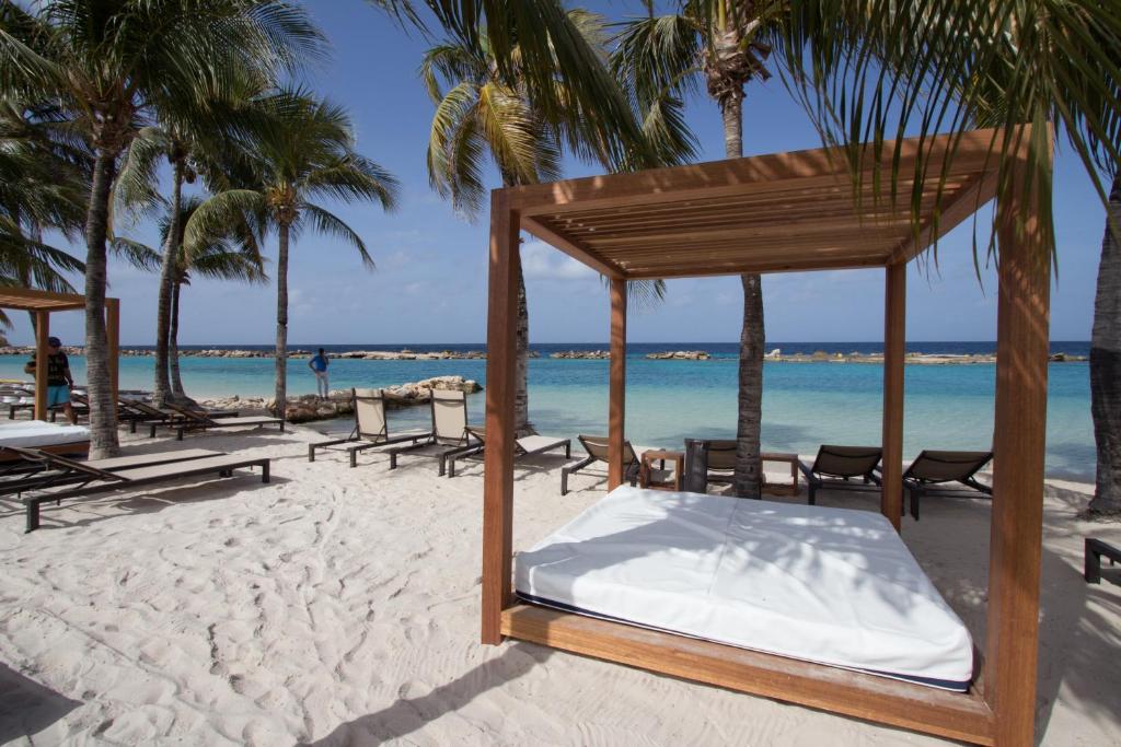 Cama en una playa con palmeras y océano en Bon Bini Seaside Resort Curacao en Willemstad