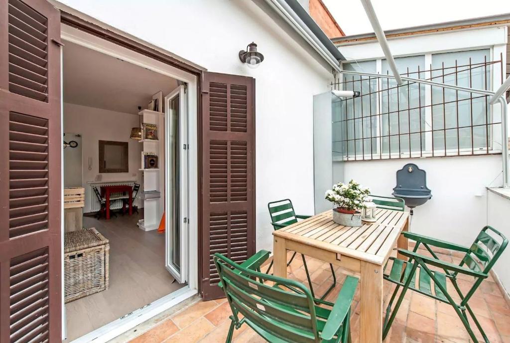 un patio con mesa de madera y sillas verdes en L'Attichetto di Ponte Milvio, en Roma