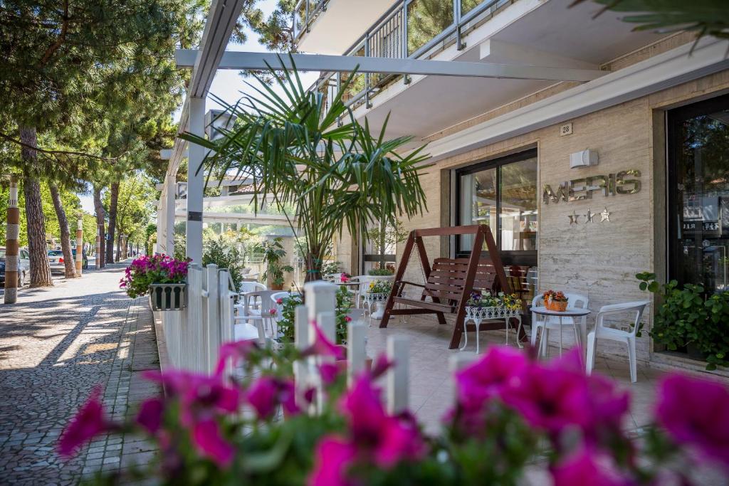 un patio con mesas, sillas y flores rosas en Hotel Meris, en Milano Marittima