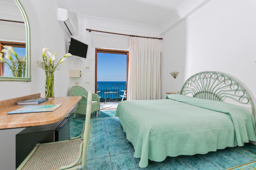 a bedroom with a bed and a desk and a view of the ocean at Hotel Pupetto in Positano