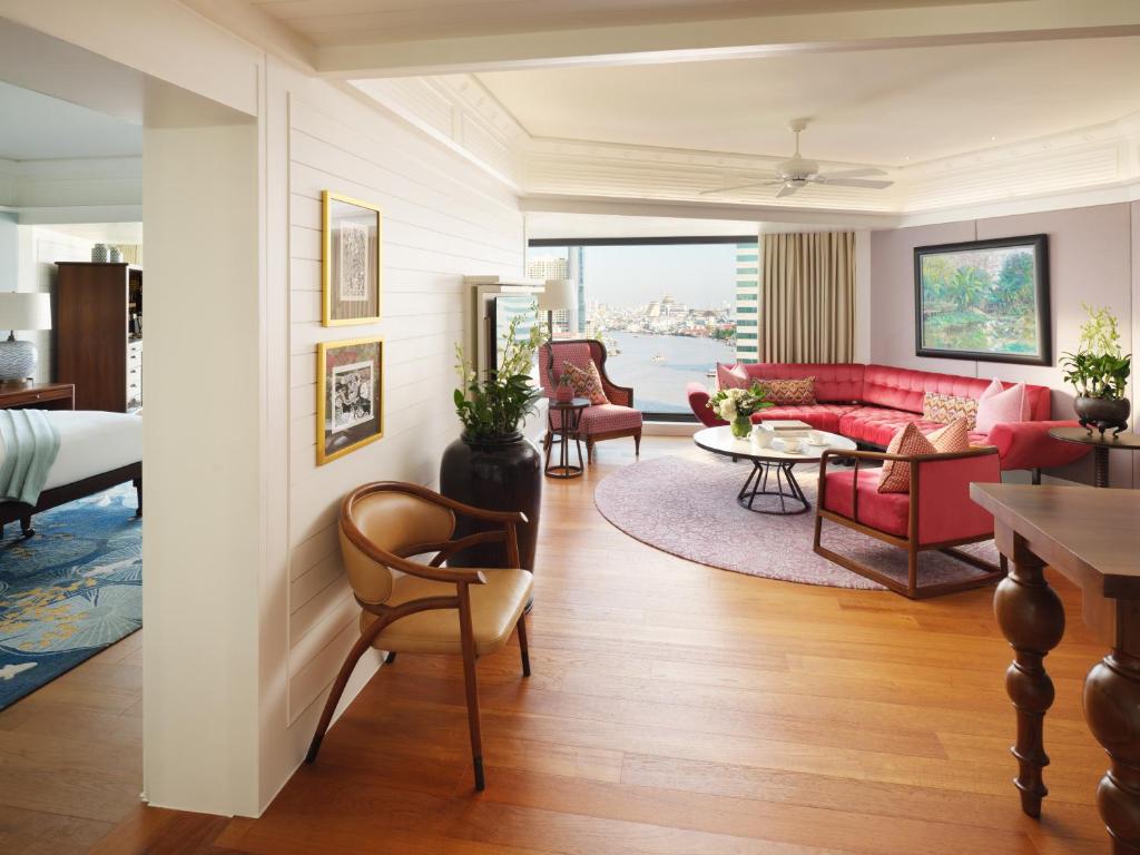 A broad suite living room with red seating, a coffee table and a distant city view.