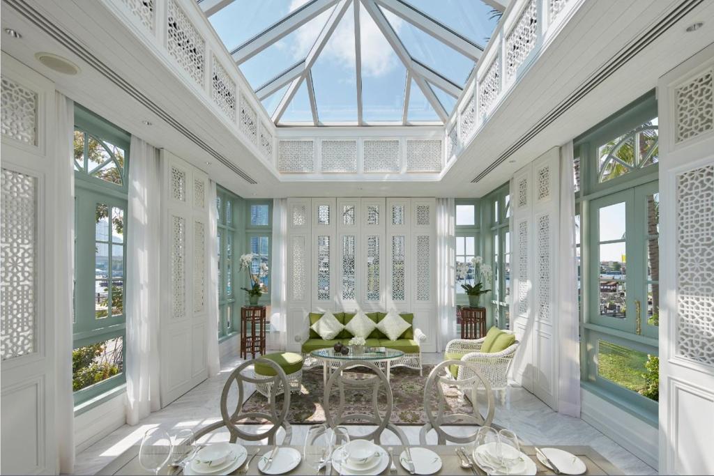 A glass-roofed conservatory dining room with garden-facing windows and a small lounge area.