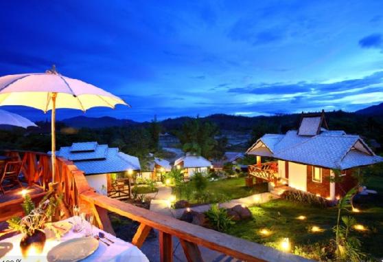 a balcony with an umbrella and a house with a view at Pai Love & Baan Chonphao Resort in Pai