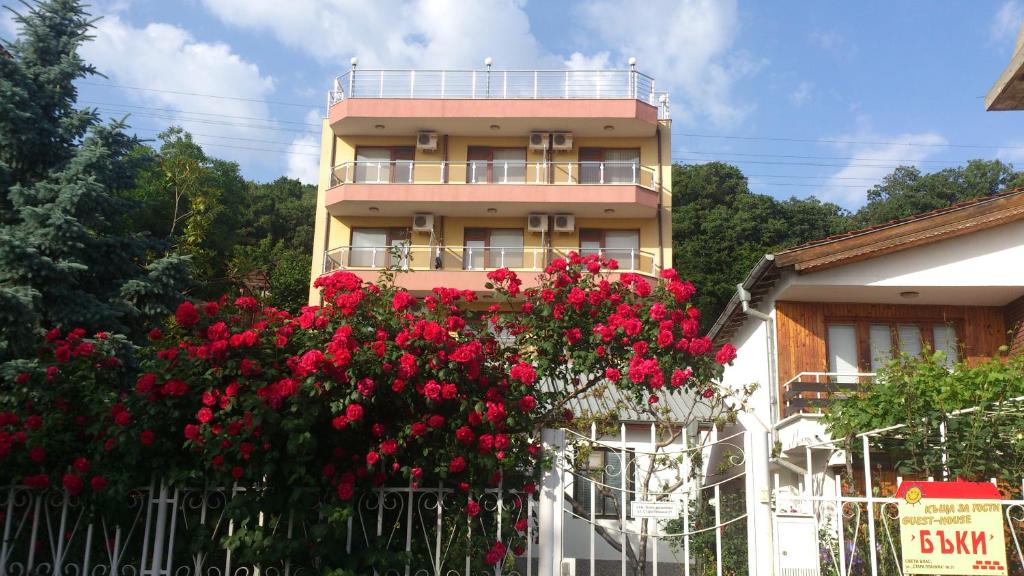 a building with red flowers in front of a fence at Guest House Byki in Sveti Vlas