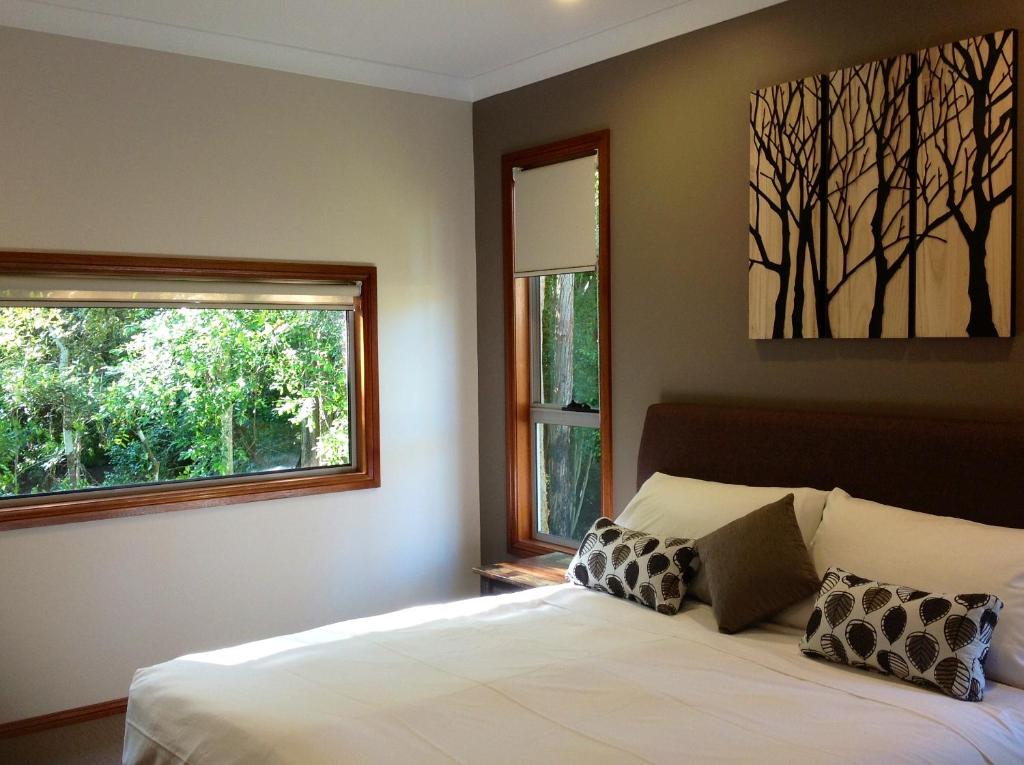 a bedroom with a bed and two windows at Mistinthegumtrees Eco Luxury Cabins in Cooranbong