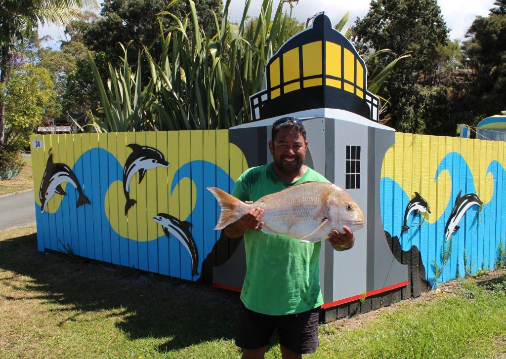 a man holding a fish in front of a lighthouse at Pukenui Holiday Park in Pukenui