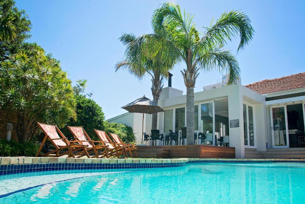 
a beach with a pool, chairs, and a balcony at First Avenue Guesthouse in Port Elizabeth
