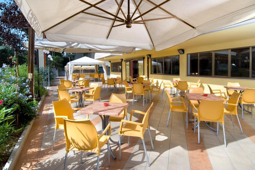 un patio al aire libre con mesas, sillas y una sombrilla en Hotel Levante, en Cervia