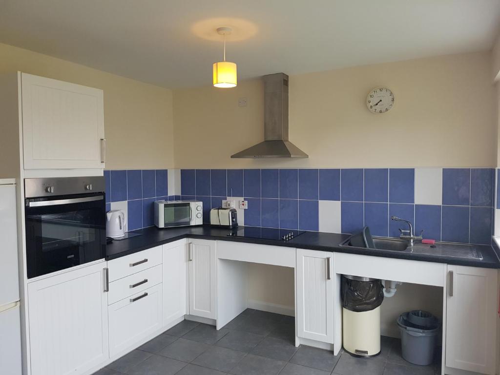 a kitchen with white cabinets and a blue tiled wall at Ingoldale House in Ingoldmells