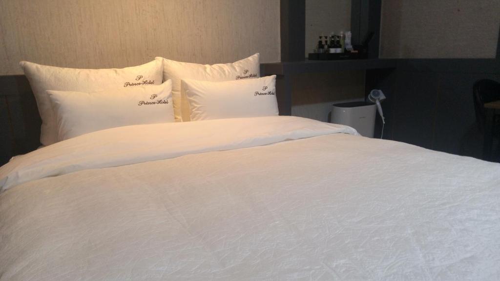 uma grande cama branca com lençóis e almofadas brancos em Hotel Prince em Busan