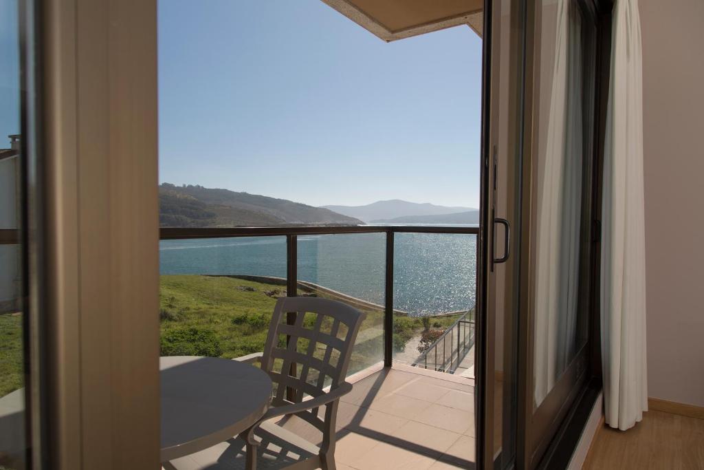 einen Balkon mit einem Tisch und Blick auf das Wasser in der Unterkunft Apartamentos Turísticos Playa de Osmo in Corme-Puerto