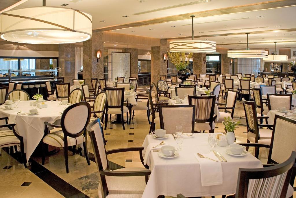a dining room with white tables and chairs and chandeliers at Grande Real Villa Itália Hotel & Spa in Cascais
