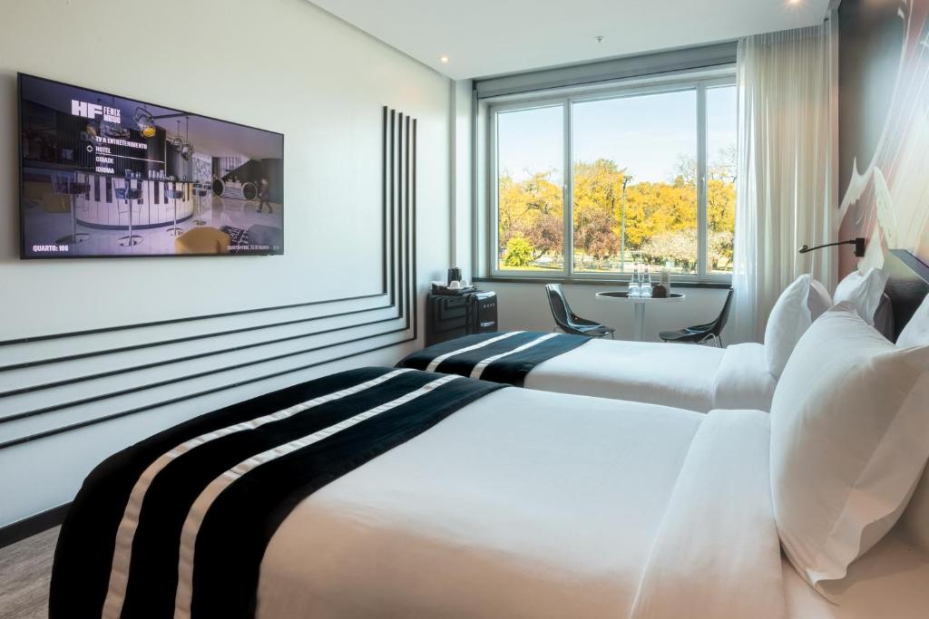 A bright twin room with a broad window, television, and compact seating area.