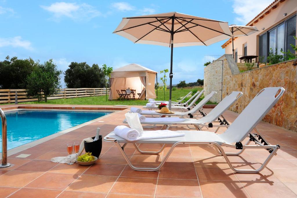 patio z krzesłami i parasolem przy basenie w obiekcie Kivotos Villa w mieście Maroulás