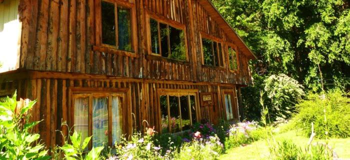 an old wooden house with flowers in front of it at Hospedaje y Agrocamping Relmucura in Melipeuco