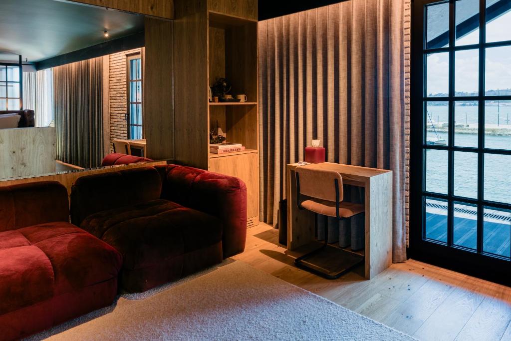 A sitting area with a deep red sofa, compact desk and waterfront-facing glass door.