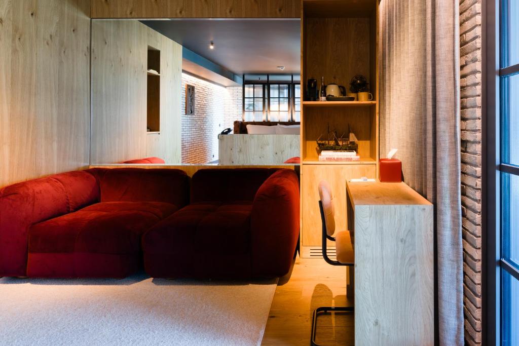 A lounge with a large red sofa, built-in kitchenette shelving and a narrow desk.