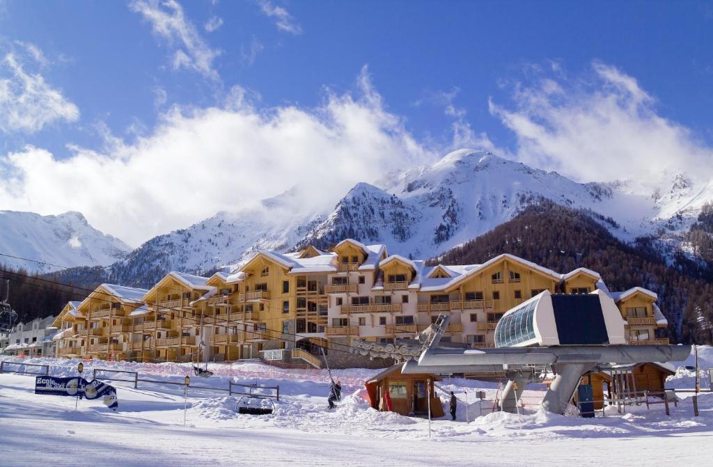 un gran edificio en la nieve con montañas en el fondo en Madame Vacances Résidence Le Parc Des Airelles, en Les Orres