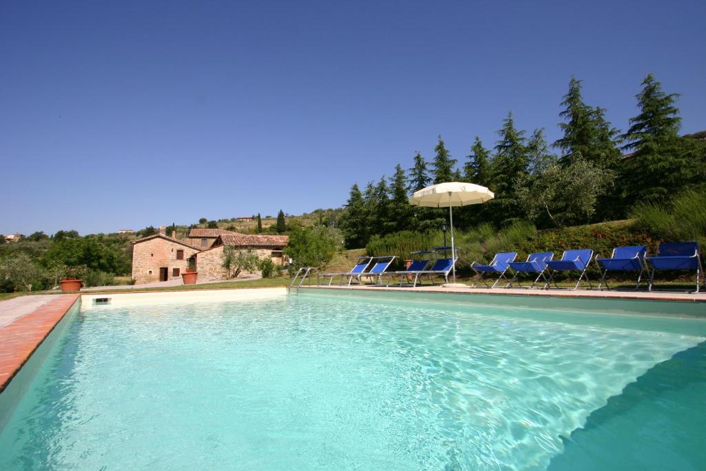 a large swimming pool with chairs and an umbrella at Villa Fontocchio in Cortona