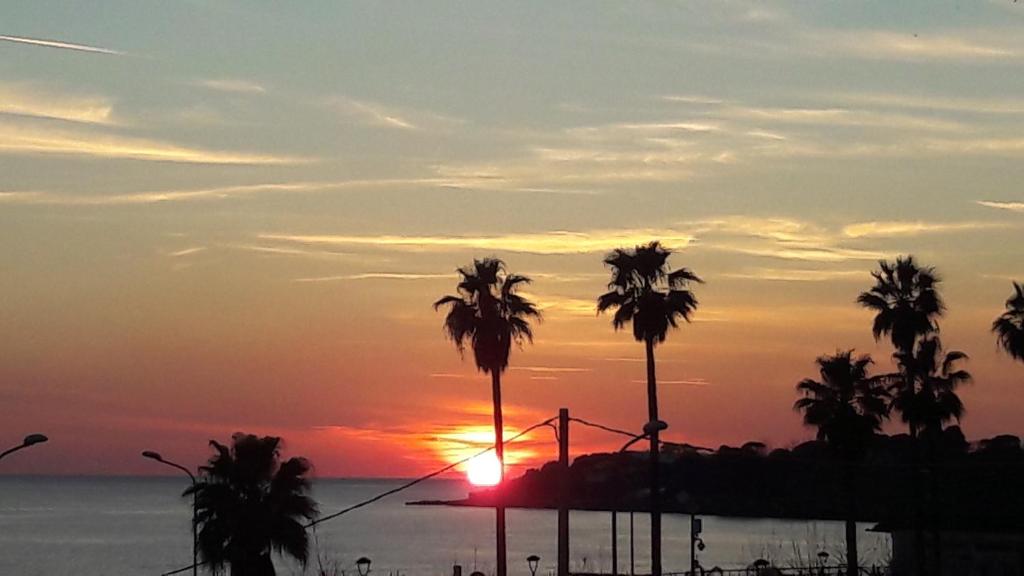 einen Sonnenuntergang mit Palmen vor dem Meer in der Unterkunft Apartment MariLù in Torre Annunziata